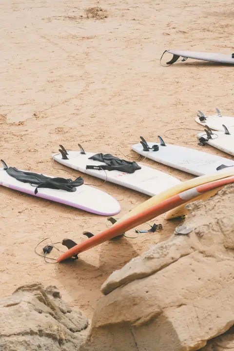 Surfboards and wetsuits laid out on the sand