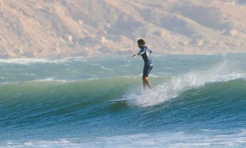 Longboarder trimming a green wave below the cliffs
