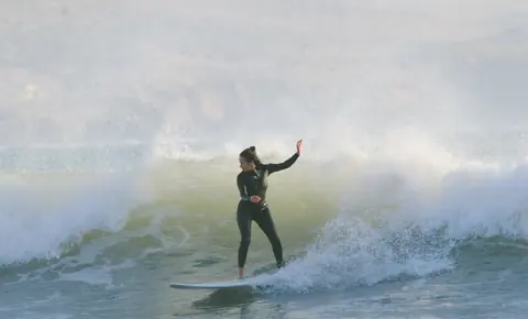 Surfer riding a wave with spray behind her